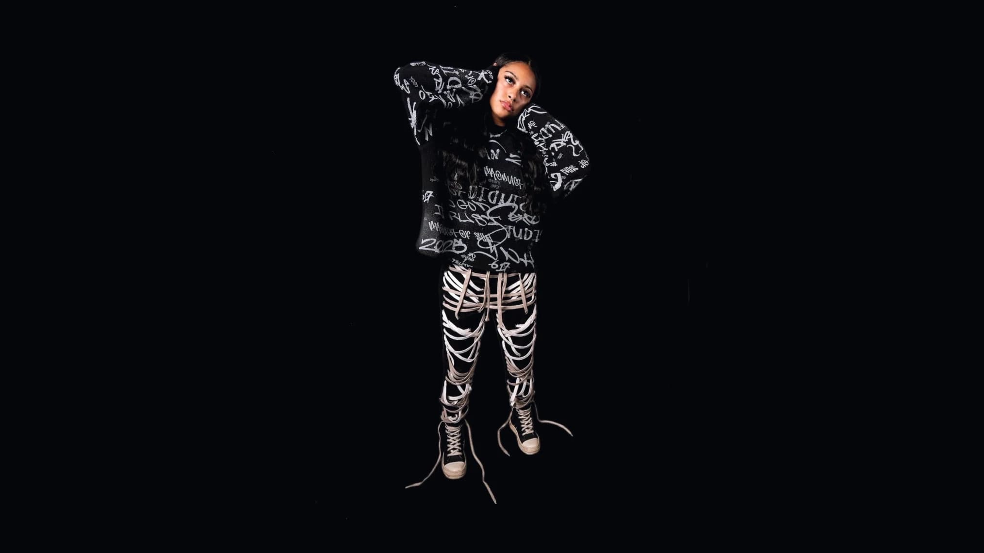 ARCHIVE26 worn: the model stands against black, hands behind her head, in the black waffle thermal with its all-over white script print